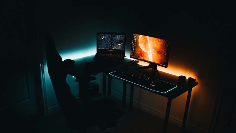 Ergonomic black gaming recliner with RGB footrest and lumbar support in a modern dark-themed home office setup
